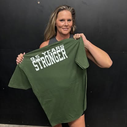 ITS member holding up a green 9.5 Years Stronger shirt at the gym